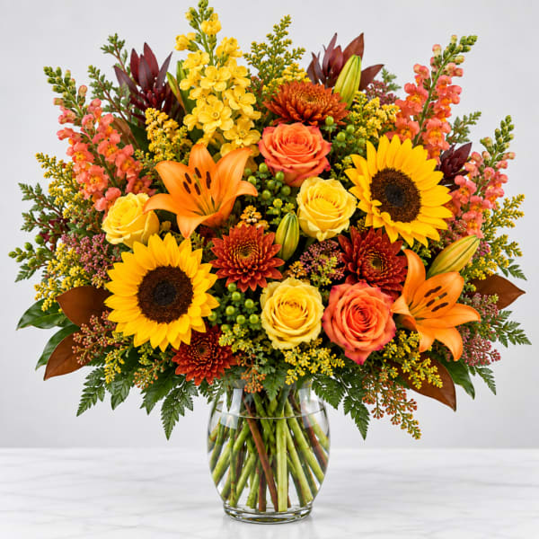 Bright mixed bouquet with sunflowers, roses, lilies, and chrysanthemums in a glass vase