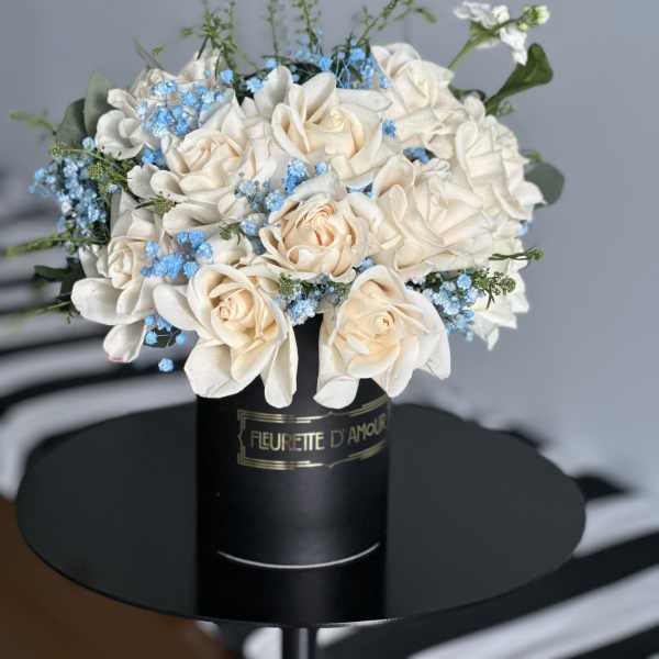 Cream roses and blue filler flowers in a black hatbox