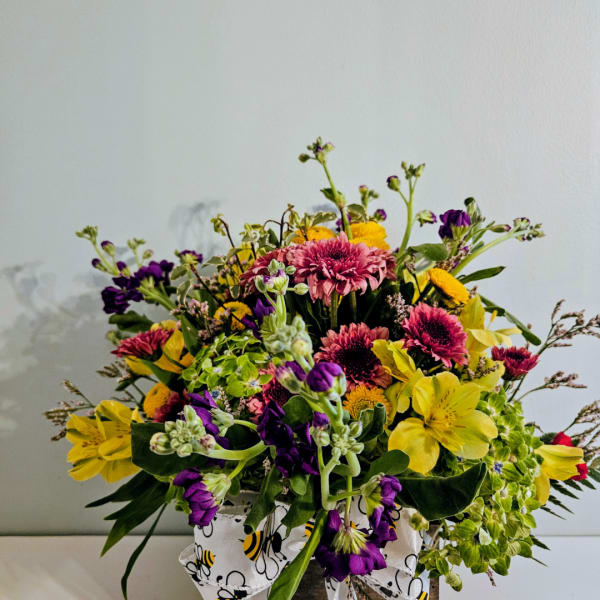 Mixed bouquet of yellow, pink, and purple flowers in a bee-patterned container