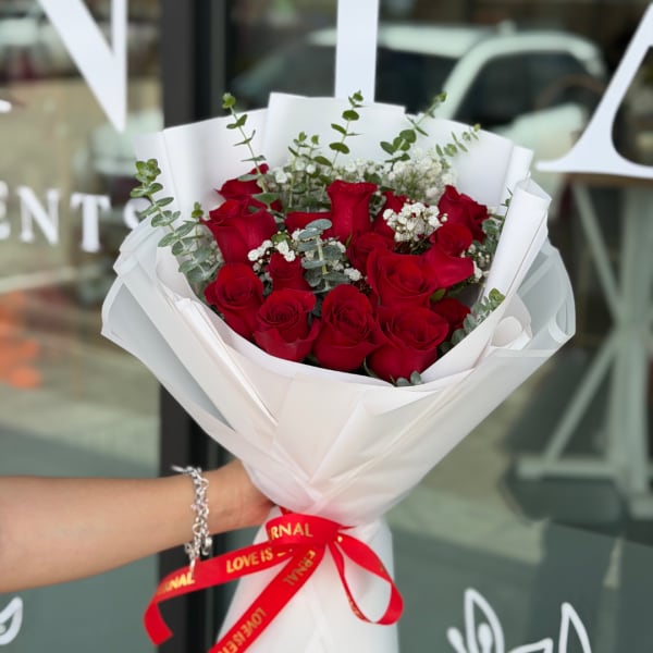 Handheld bouquet of red roses wrapped in white paper with a red ribbon