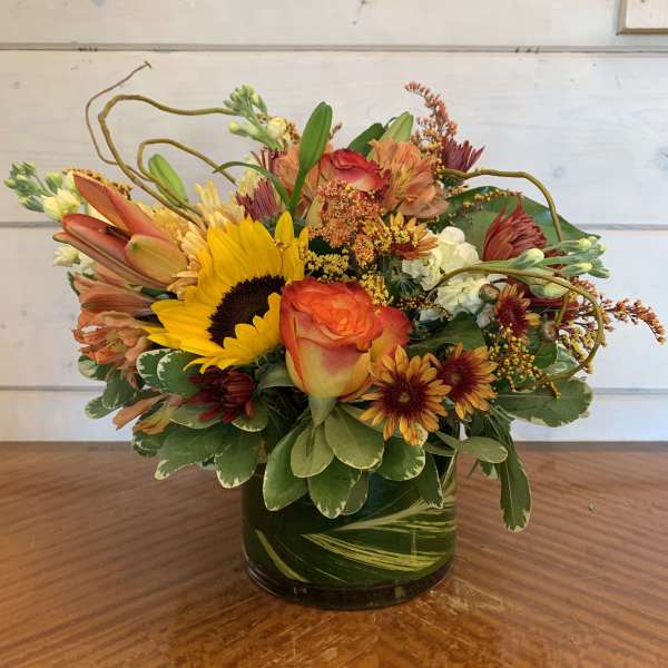 Mixed bouquet with sunflowers, roses, and lilies in a glass vase