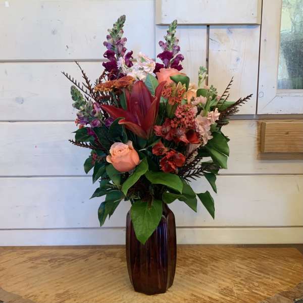 Mixed bouquet in a dark glass vase with pink, red, and purple blooms