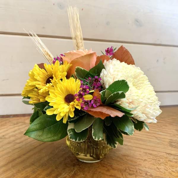 Yellow daisies and white chrysanthemum in a glass vase with peach rose accents