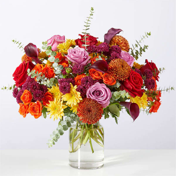 Mixed bouquet of roses, chrysanthemums, and calla lilies in a clear glass vase