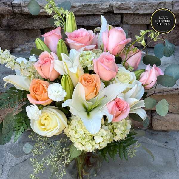 Glass vase arrangement of pink and peach roses with white lilies and hydrangea