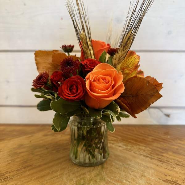 Orange and red rose arrangement in a clear glass vase