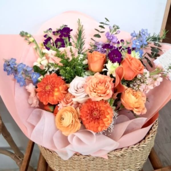 Mixed bouquet of orange, purple, and blue flowers wrapped in pink paper