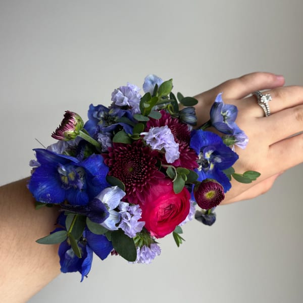 Handheld wrist corsage with blue and purple flowers and a pink rose