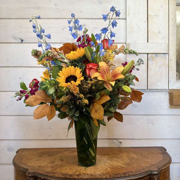 Mixed bouquet with sunflowers, lilies, and blue delphinium in a tall vase