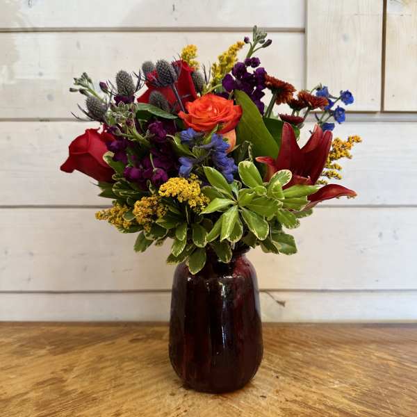 Mixed bouquet of red, orange, purple, and yellow flowers in a dark glass vase