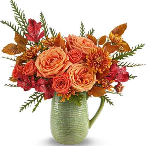 Orange and red flower arrangement in a green ceramic pitcher
