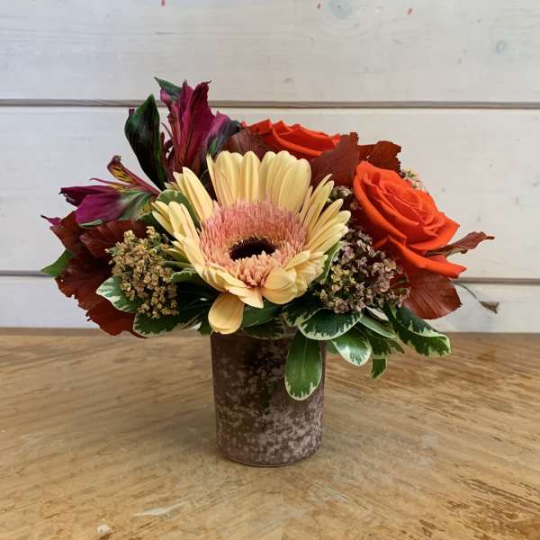 Orange roses and a pale gerbera daisy in a small vase