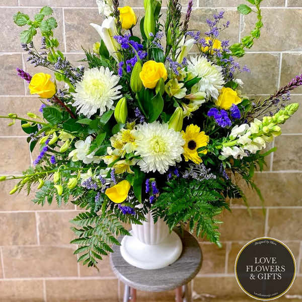 Tall yellow, white, and purple flower arrangement in a white pedestal vase