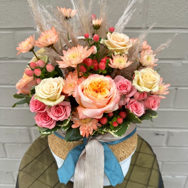 Peach and pink rose bouquet with daisies in a woven hatbox