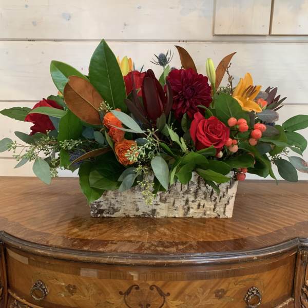 Mixed floral arrangement in a birch bark container with red, orange, and yellow blooms