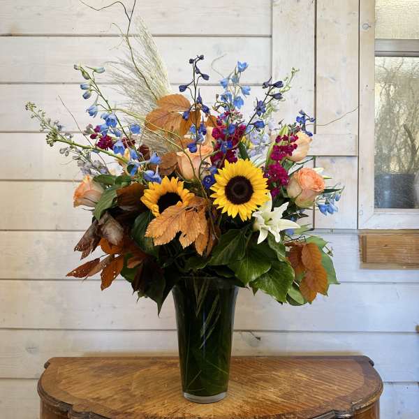 Sunflowers and mixed blooms in a tall glass vase with autumn leaves