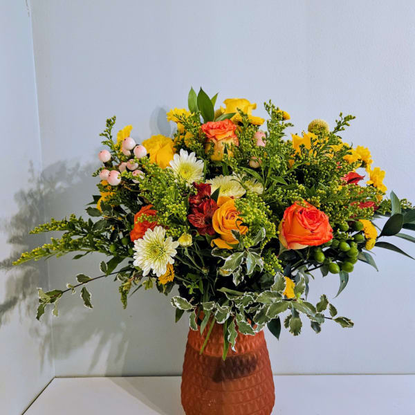 Mixed bouquet of orange, yellow, and white flowers in a textured vase