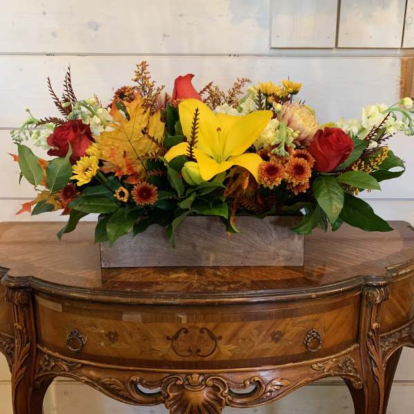 Autumn floral arrangement with yellow lilies, red roses, and orange mums in a rectangular container