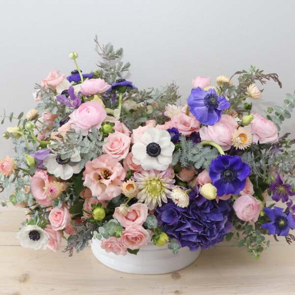 Pink and purple mixed flower arrangement in a white bowl vase