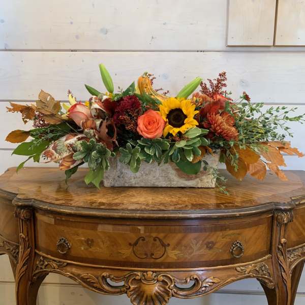 Autumn floral arrangement with a sunflower, orange rose, and pumpkins in a rectangular container