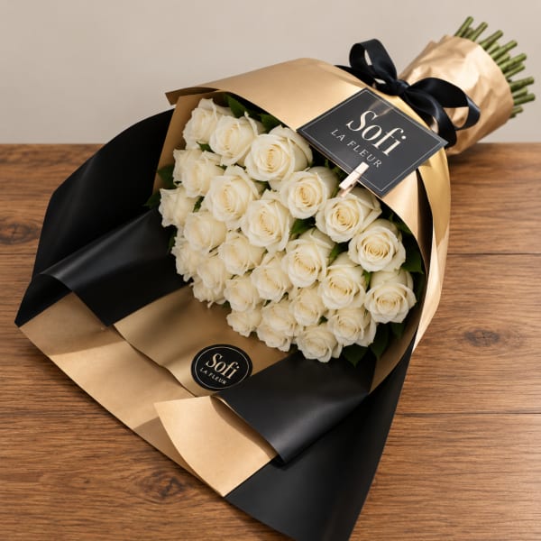 Bouquet of white roses wrapped in gold and black paper with a ribbon