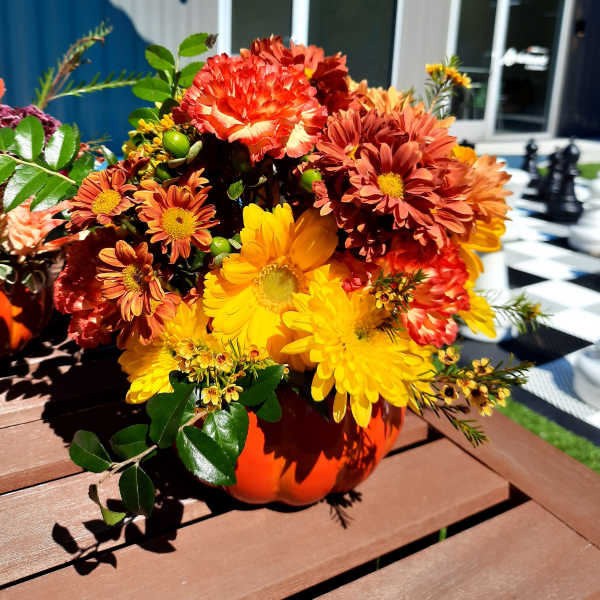 Orange and yellow chrysanthemum arrangement in a pumpkin-shaped vase