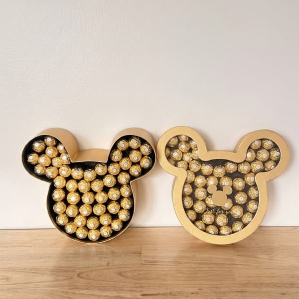 Two Mickey-shaped boxes filled with gold-wrapped chocolates on a wooden surface