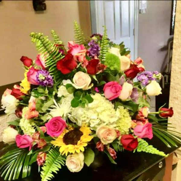Large mixed arrangement of roses, hydrangea, sunflower and other blooms in a low container