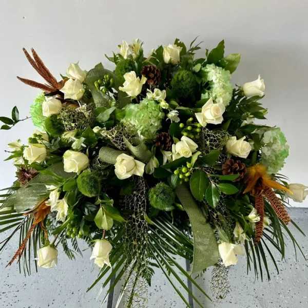 Large spray of white roses and green blooms with pinecones and feathers on palm fronds.