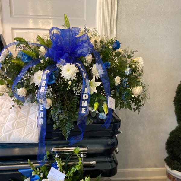 Blue and white funeral spray on a casket with ribbon streamers
