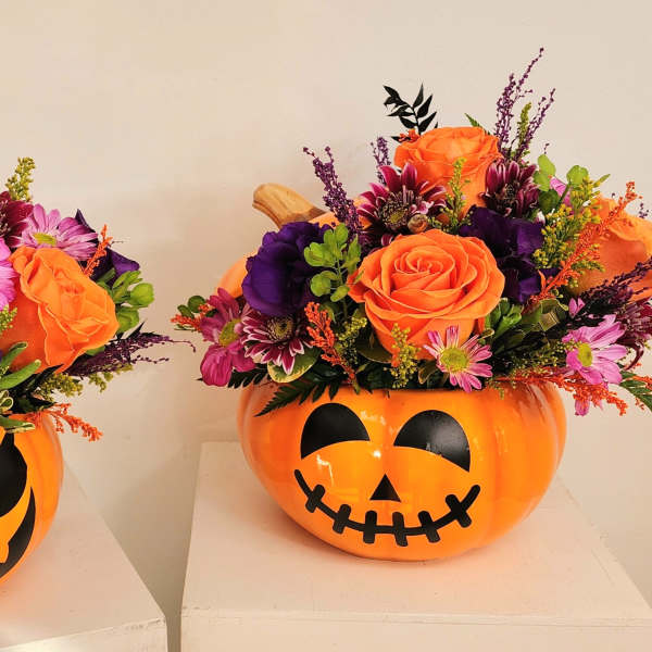 Two orange jack-o'-lantern containers filled with mixed flowers