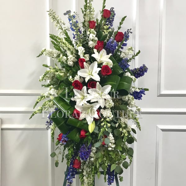 Tall standing floral spray with red roses, white lilies, and blue flowers