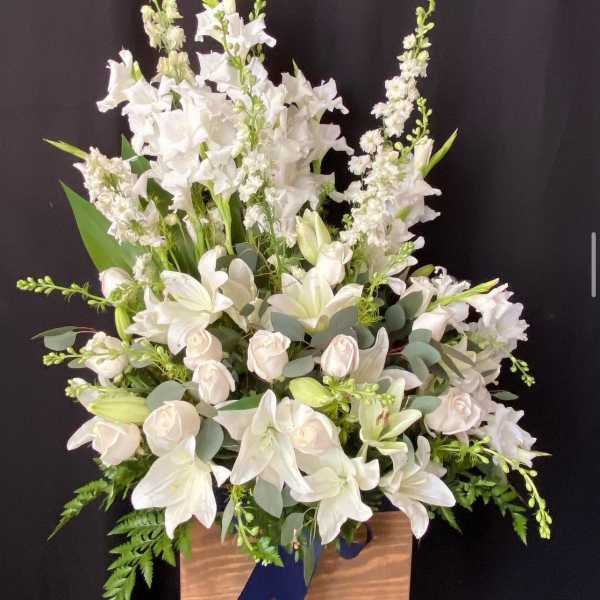 White floral arrangement in a wooden stand with a blue ribbon