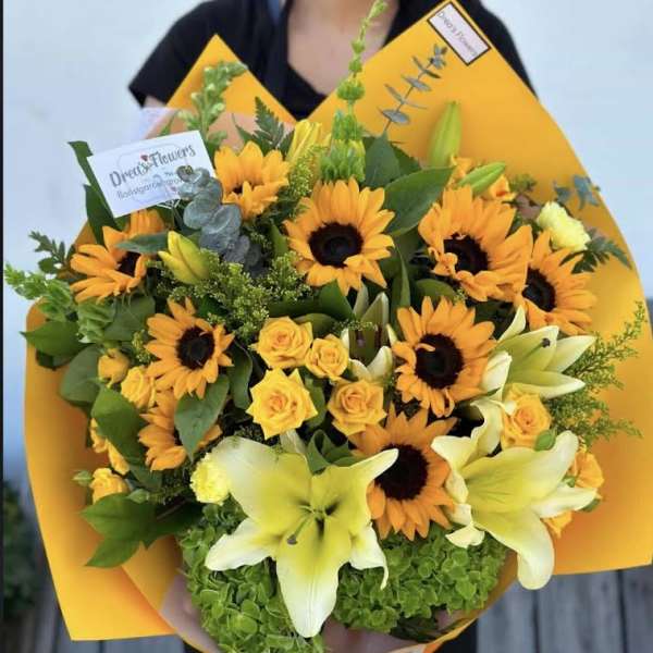 Bouquet of yellow sunflowers, roses, and lilies wrapped in bright orange paper