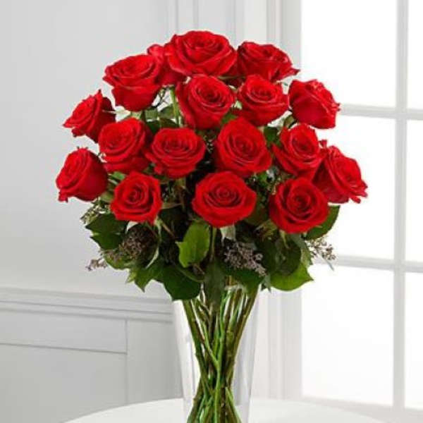 Tall clear vase filled with long-stemmed red roses.