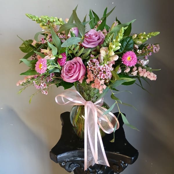 Pink roses and mixed blooms arranged in a glass vase with a ribbon
