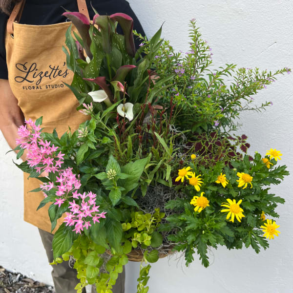 Person holding a large mixed floral basket with pink, yellow, and white blooms