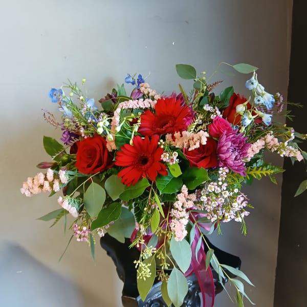 Mixed bouquet with red gerbera daisies, red roses, and pink flowers in a dark vase