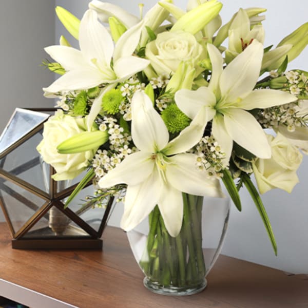 White lilies and roses arranged in a clear glass vase