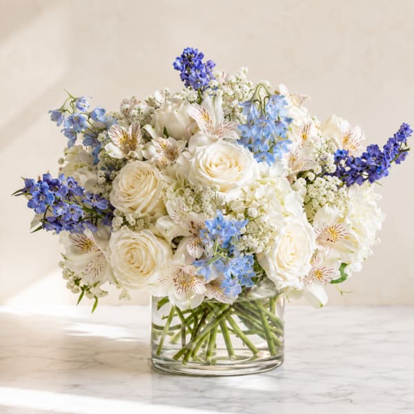 White roses and blue flowers arranged in a clear glass vase