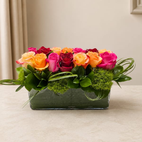 Mixed roses in a low rectangular glass vase with green accents