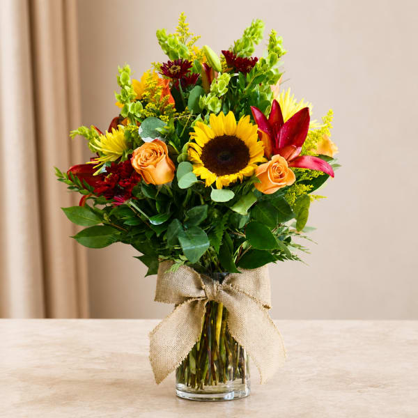 Mixed bouquet with sunflowers, roses, and lilies in a glass vase