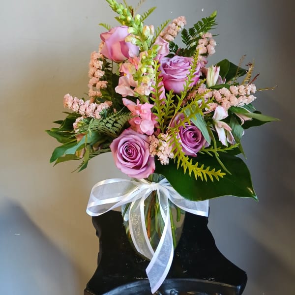 Pink and lavender roses arranged in a glass vase with a white ribbon