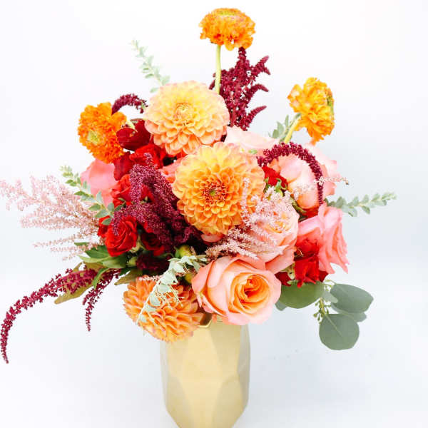 Bouquet of orange, pink, and red flowers in a gold vase