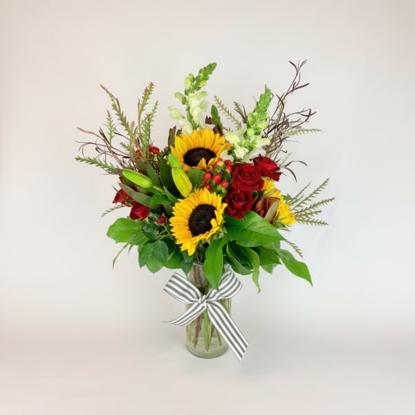 Sunflowers and red roses in a glass vase with a striped ribbon