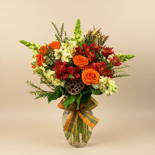 Orange roses and red alstroemeria in a glass vase with a plaid ribbon