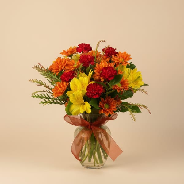 Bouquet of orange, yellow, and red flowers in a glass vase with a ribbon