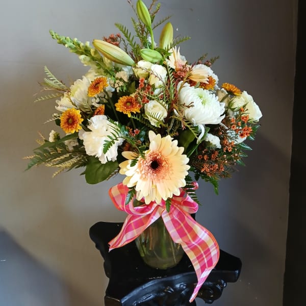 Mixed bouquet of white and peach flowers in a glass vase with a pink plaid ribbon