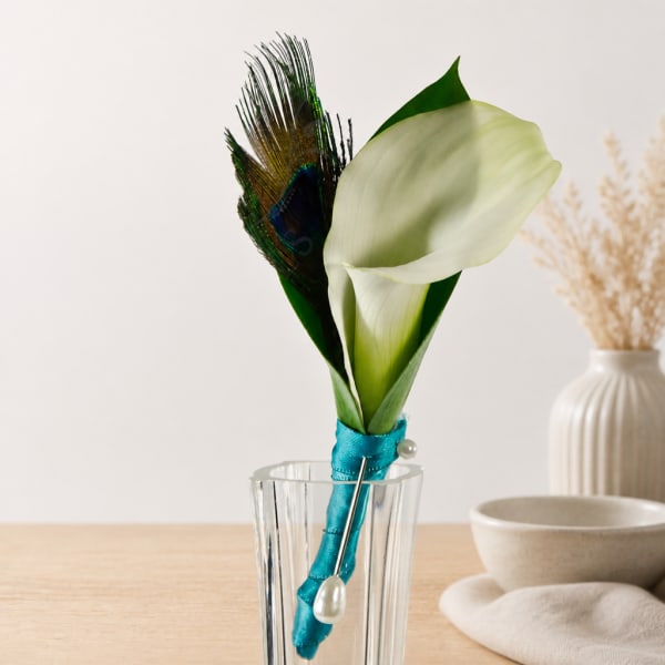 White calla lily boutonniere with a peacock feather in a glass vase