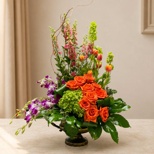 Orange roses and purple orchids in a low vase with tall pink blooms